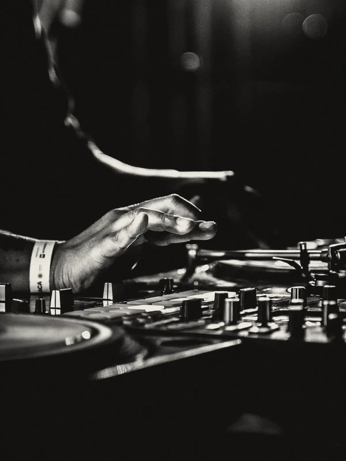 Manos de un DJ sobre el mixer y el plato, en cabina con poca luz